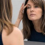 Woman examining her skin in the mirror after NeoGen or Plexr plasma treatment.