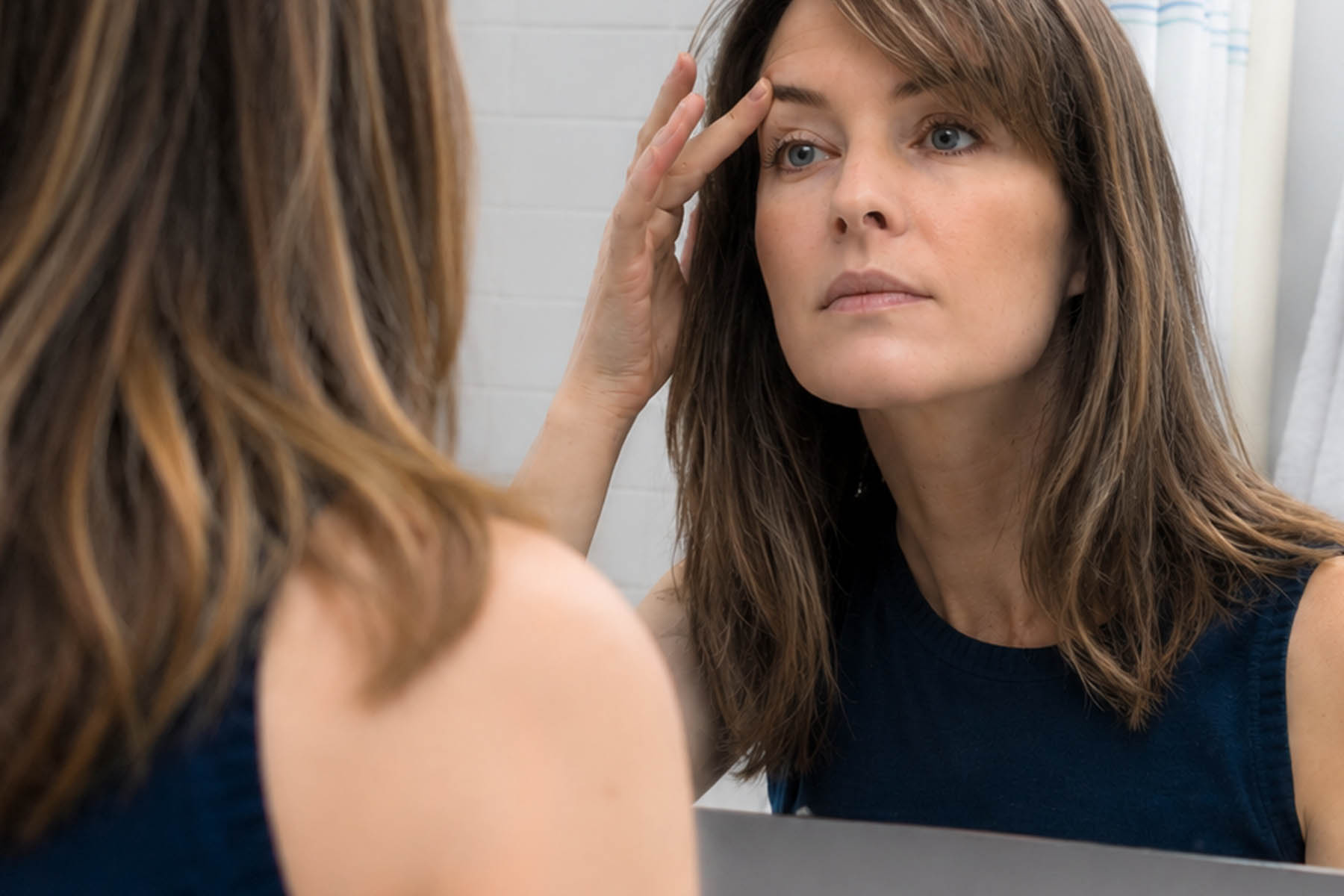 Woman examining her skin in the mirror after NeoGen or Plexr plasma treatment.