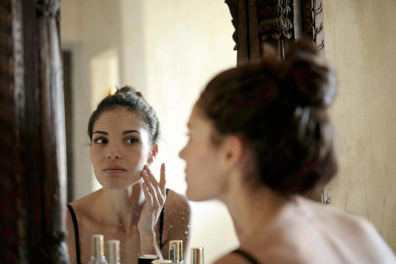 Woman examining her facial skin in a mirror while touching her cheek