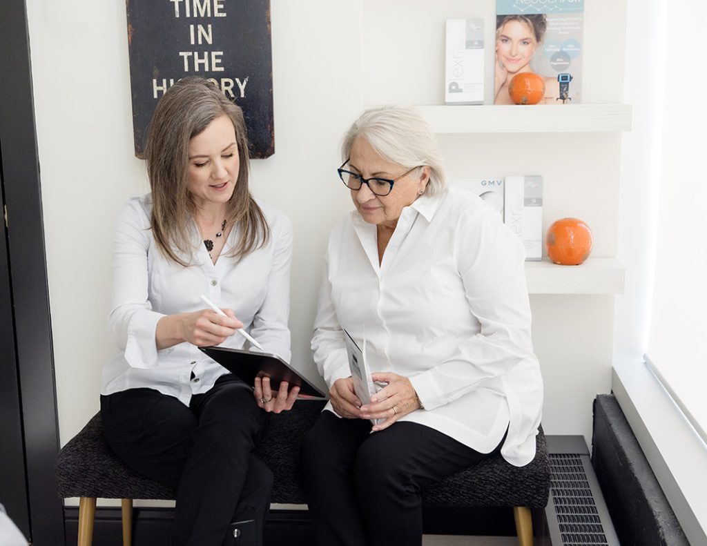 Two women reviewing information on a tablet during a NeoGen plasma treatment consultation in a medical aesthetics clinic