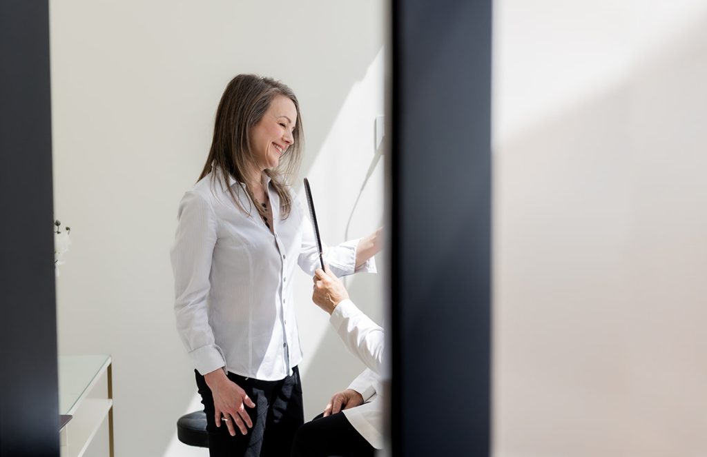 Woman speaking with a client seated in a medical aesthetics chair, photographed through a clinic doorway