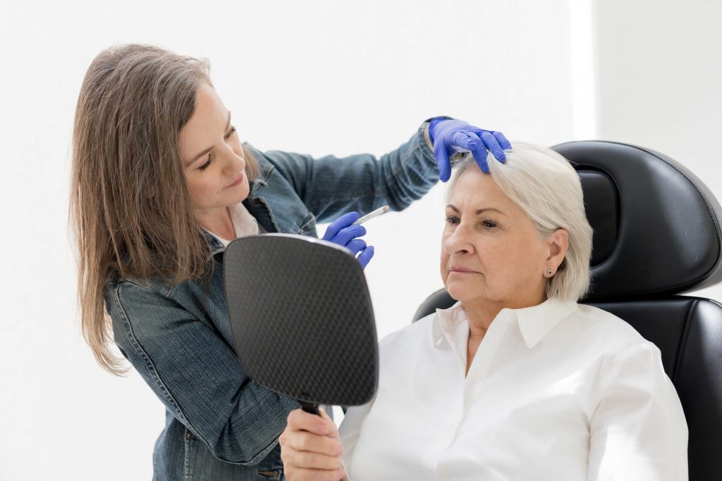 Practitioner assessing mature facial skin during a NeoGen plasma consultation as client looks in a mirror