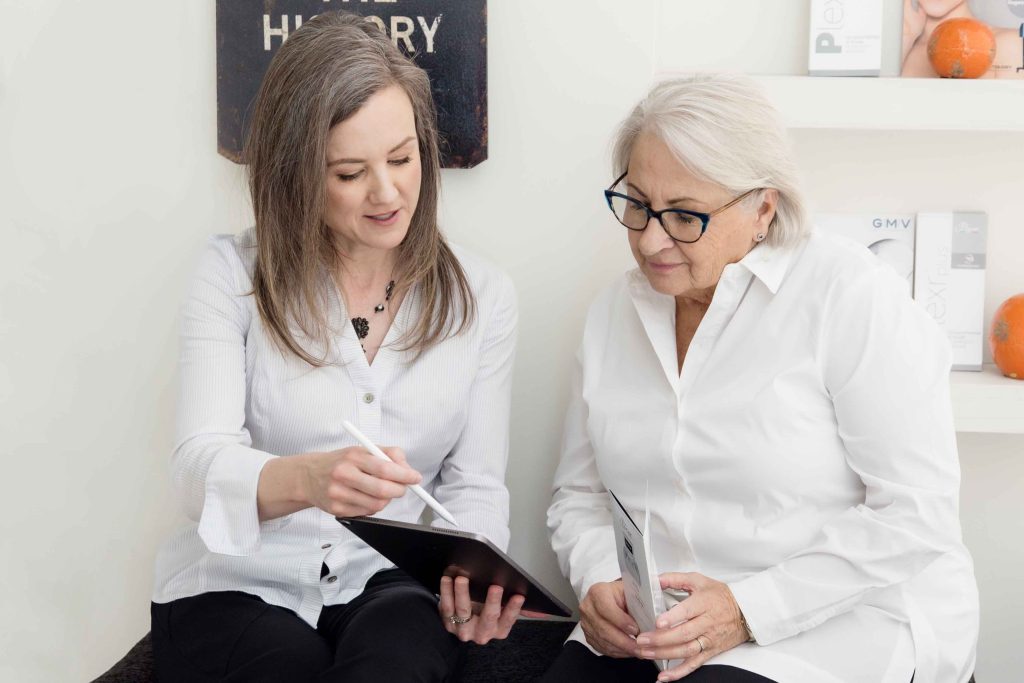 Two women reviewing information on a tablet during a NeoGen plasma treatment consultation in a medical aesthetics clinic