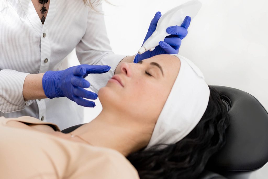 Woman undergoing a non-surgical plasma skin treatment while resting on an aesthetic treatment bed.