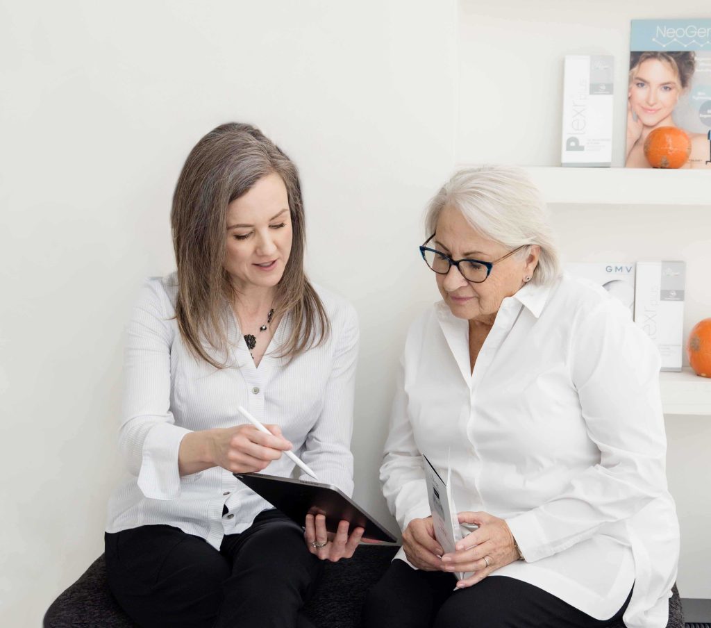 Two women reviewing information on a tablet during a NeoGen plasma treatment consultation in a medical aesthetics clinic