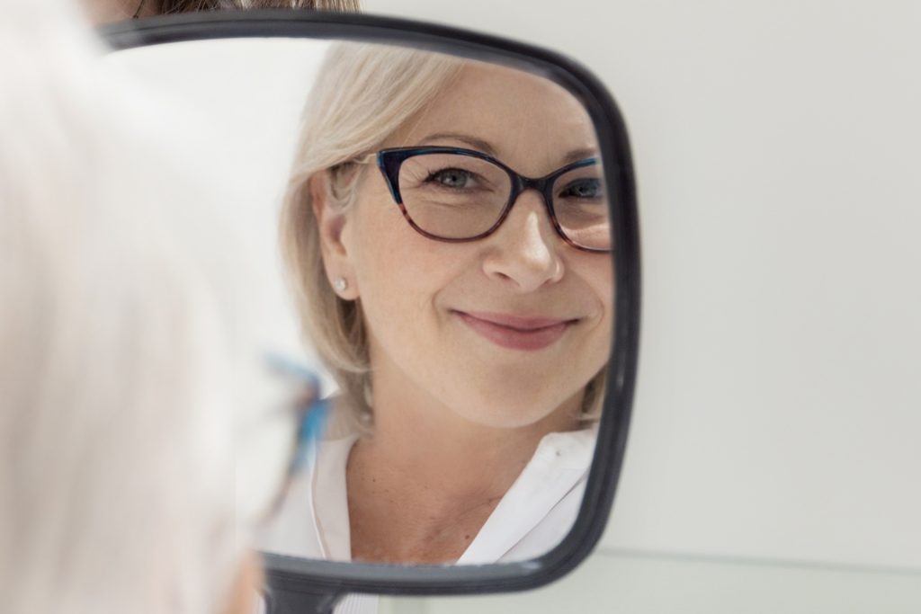 Woman looking at her reflection after NeoGen plasma skin renewal treatment in Calgary, showing naturalcollagen remodeling