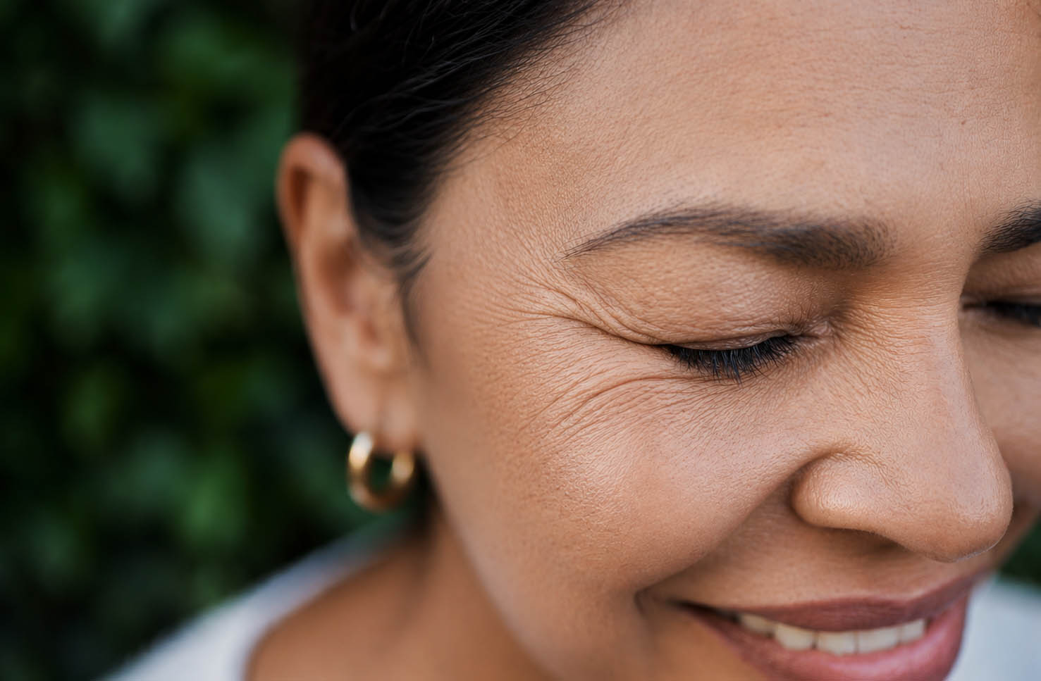 Close-up of a smiling middle-aged woman showing natural crow's feet and fine lines around the outer eye area.