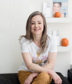 Sarah, registered nurse and medical aesthetics clinic owner, seated in her clinic and smiling
